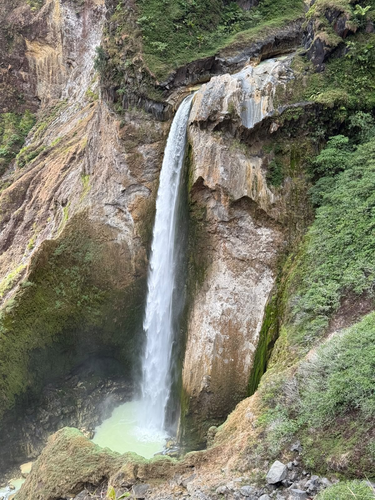 A tall waterfall plunging down a wall of the Torean canyon into a pale green plunge pool on the descent